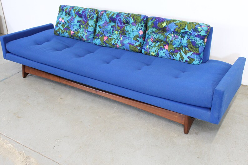 May include: A blue tufted sofa with a wooden frame and three floral patterned throw pillows.