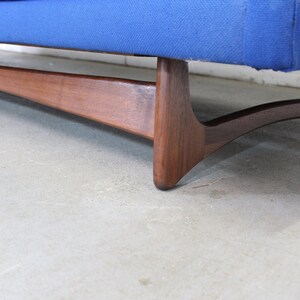 May include: A blue fabric sofa with a wooden frame and legs. The legs are angled and have a unique design.
