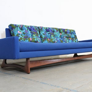 May include: A blue mid-century modern sofa with a wood frame and floral patterned cushions.