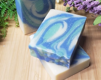 May include: Three bars of handmade soap with a blue and white swirl pattern. The soap is on a light wood surface.