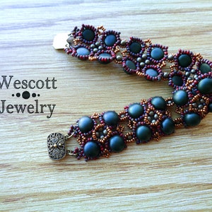 May include: A beaded bracelet with dark green and burgundy beads. The bracelet features a repeating pattern of dark green beads surrounded by smaller burgundy and bronze-colored beads. The clasp is a decorative rectangle with an ornate design. The text "Wescott Jewelry" is visible.