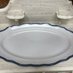 May include: Oval white serving platter with a scalloped edge and a dark blue border. The platter has decorative dark accents on each end. A classic piece for serving food.