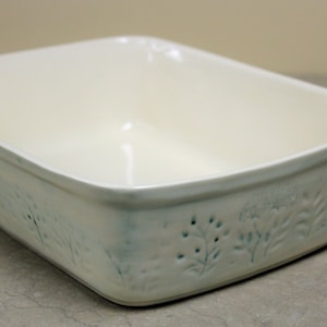 May include: Off-white rectangular ceramic baking dish with embossed floral and leaf patterns. The dish has a slightly textured surface and a light blue-green accent color on the embossed details.