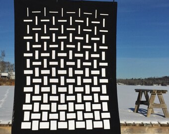 Könnte beinhalten: Ein schwarzer Stoffhintergrund mit einem weißen geometrischen Muster aus gewebten Quadraten. Der Hintergrund hängt an einer Holzkonstruktion und befindet sich vor einer schneebedeckten Landschaft.