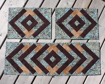 Könnte beinhalten: Ein Set aus drei gesteppten Tischsets in einem geometrischen Muster. Die Tischsets sind braun, beige und blaugrün mit einem wirbelnden Muster.