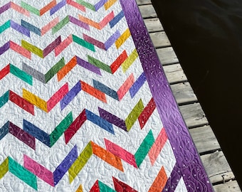 Könnte beinhalten: Eine bunte Chevron-Steppdecke mit einem violetten Rand und einem weißen Hintergrund. Die Steppdecke ist aus verschiedenen Stoffen in verschiedenen Farben und Mustern gefertigt. Die Steppdecke ist mit einem wirbelnden Muster gesteppt.