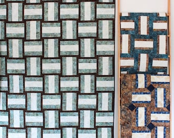 Könnte beinhalten: Zwei Quilts mit einem geometrischen Muster aus braunen, weißen und blauen Quadraten. Die Quilts hängen an einer weißen Wand.