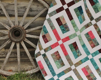 Könnte beinhalten: Eine weiße Steppdecke mit Patchwork-Muster aus Quadraten in Teal, Braun und Pink. Die Steppdecke ist gefaltet und lehnt an einem hölzernen Wagenrad.