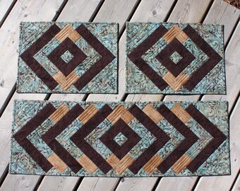 Könnte beinhalten: Set aus drei gequilteten Tischsets in einem geometrischen Muster mit braunen, beigefarbenen und blaugrünen Farben. Die Tischsets sind aus Stoff und haben ein gestepptes Design.