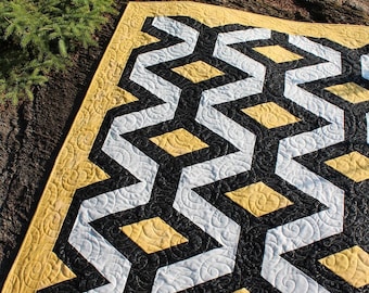 Könnte beinhalten: Eine Steppdecke mit einem geometrischen Muster in Schwarz, Weiß und Gelb. Die Steppdecke besteht aus Stoffquadraten, die zusammengenäht wurden, um ein sich wiederholendes Muster aus Rauten und Zickzacklinien zu erzeugen.