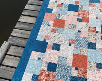 Könnte beinhalten: Eine Patchwork-Decke mit blauem Rand und verschiedenen floralen und geometrischen Mustern in Blautönen, Rosa und Orange.