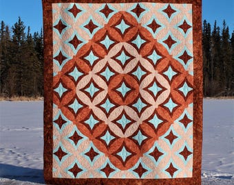 Könnte beinhalten: Eine Steppdecke mit einem geometrischen Muster aus braunen, blauen und rosafarbenen Diamanten und Kreisen. Die Steppdecke wird vor einem schneebedeckten Hintergrund gezeigt.