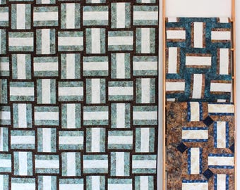 Könnte beinhalten: Zwei Quilts mit einem geometrischen Muster aus braunen, weißen und blauen Quadraten. Die Quilts hängen an einer weißen Wand.