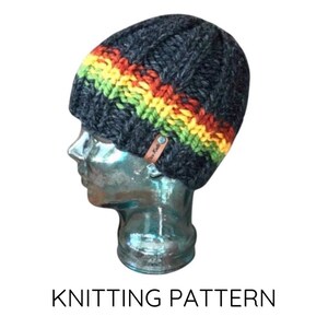 May include: A dark gray knit beanie with a horizontal stripe of yellow, green, and red. The hat is displayed on a mannequin head. A small brown tag is attached to the side of the hat. The text "KNITTING PATTERN" is below the hat.
