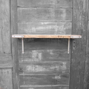 May include: A wooden shelf with metal brackets mounted on a gray wooden wall. The shelf has the letters "DSL" stamped on the surface.