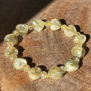 May include: A bracelet made of light yellow heart-shaped beads with smaller clear beads interspersed throughout.