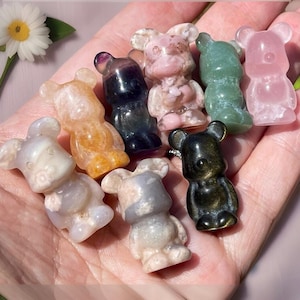 May include: A collection of eight small, carved bear figurines made from various types of polished stones. The bears are in different colors, including pink, green, black, white, and orange.