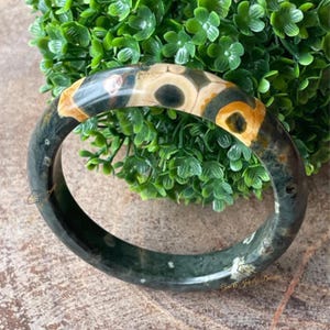 May include: A black, white, and brown agate stone bangle bracelet. The bracelet has a polished finish and is made of natural stone.