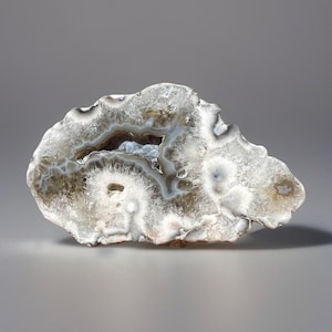 May include: A polished agate geode, showcasing a natural formation with a hollow center. The stone features bands of white, gray, and brown, creating a unique pattern. The geode is cut to reveal the crystalline interior, offering a glimpse into its geological history.