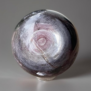 May include: A spherical, decorative glass object with a swirling, galaxy-like pattern in shades of purple, gray, and white. The glass has a glossy finish and a small, rounded base. The design resembles a nebula.