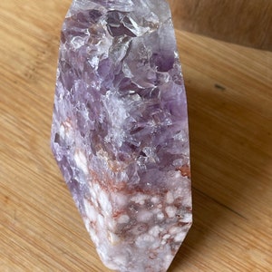 May include: A large, polished amethyst crystal point. The crystal features a gradient of colors, from a deep purple at the top to a white and reddish-brown base. The surface is textured with visible crystalline structures.