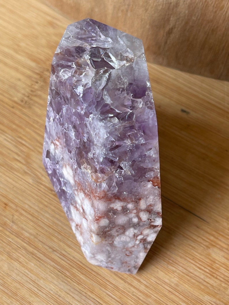 May include: A large, polished amethyst crystal point. The crystal features a gradient of colors, from a deep purple at the top to a white and reddish-brown base. The surface is textured with visible crystalline structures.