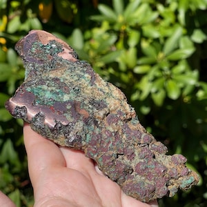 May include: A raw mineral specimen featuring a metallic copper surface transitioning into a textured, porous matrix of deep maroon, dark brown, and vibrant teal green mineral deposits across its irregular, elongated, and jagged geological form.