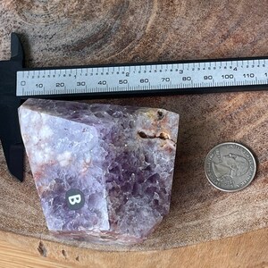 May include: A raw amethyst crystal with a quarter for size comparison. The crystal is a mix of purple, white, and brown hues. A ruler shows the crystal is approximately 4 inches long. The crystal has a rough, natural texture.