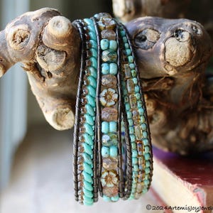 May include: A multi-strand wrap bracelet featuring turquoise and brown beads, with floral accents. The bracelet is wrapped with dark wire and is displayed on a piece of driftwood. The bracelet is a unique piece of jewelry.