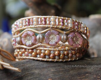 May include: A multi-layered leather wrap bracelet with pink and gold flower beads. The bracelet is made with a variety of beads and leather cord.