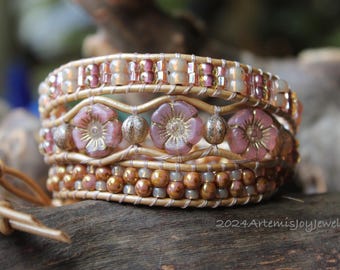 May include: A multi-layered leather wrap bracelet with pink and gold flower beads. The bracelet is made with a variety of beads and leather cord.