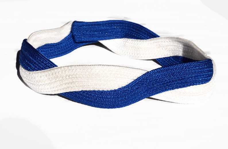 May include: A braided headband in a twisted design, featuring alternating bands of white and royal blue. The headband is made of a woven material and is shown against a white background.