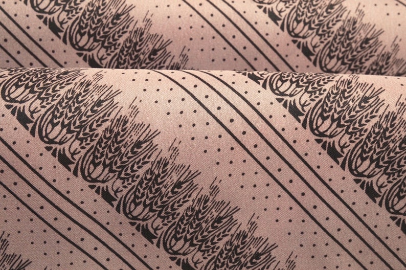 Puede incluir: Primer plano de tela con un patr&oacute;n repetido de espigas de trigo negras, rayas diagonales y peque&ntilde;os puntos sobre un fondo rosa apagado. La tela est&aacute; doblada, mostrando m&uacute;ltiples capas del dise&ntilde;o. El tema general es agr&iacute;cola o r&uacute;stico.