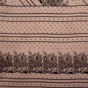 Puede incluir: Primer plano de una tela con un patr&oacute;n repetitivo. El dise&ntilde;o presenta rayas horizontales, filas de puntos y espigas de trigo estilizadas en negro sobre un fondo beige. La tela tiene una textura suave.