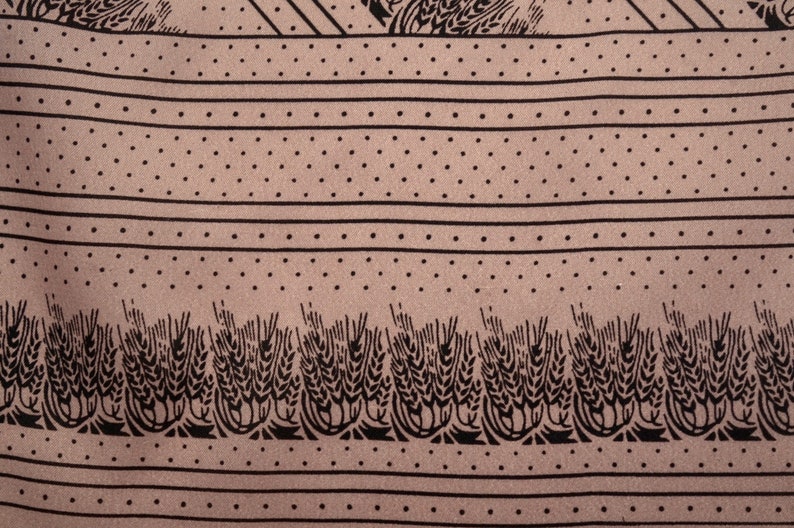 Puede incluir: Primer plano de una tela con un patr&oacute;n repetitivo. El dise&ntilde;o presenta rayas horizontales, filas de puntos y espigas de trigo estilizadas en negro sobre un fondo beige. La tela tiene una textura suave.