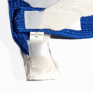 May include: Close-up of a blue and white hat with a hook and loop fastener. The hat has a blue band and a white section. A tag is visible with text that reads "MADE IN TAIWAN".