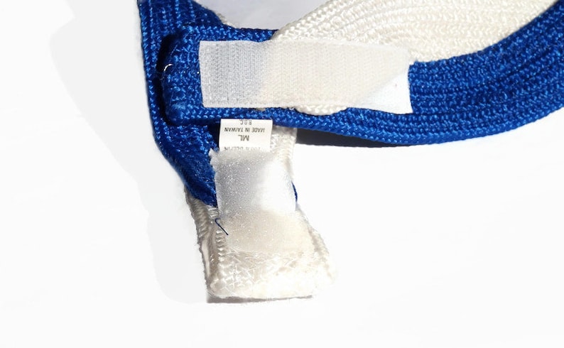May include: Close-up of a blue and white hat with a hook and loop fastener. The hat has a blue band and a white section. A tag is visible with text that reads "MADE IN TAIWAN".