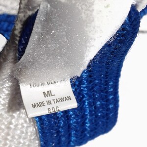 May include: Close-up of a white and blue knitted textile. A white label with black text reads "100% OLEFIN", "ML", "MADE IN TAIWAN R.O.C.". The textile has a textured appearance with a blue border.