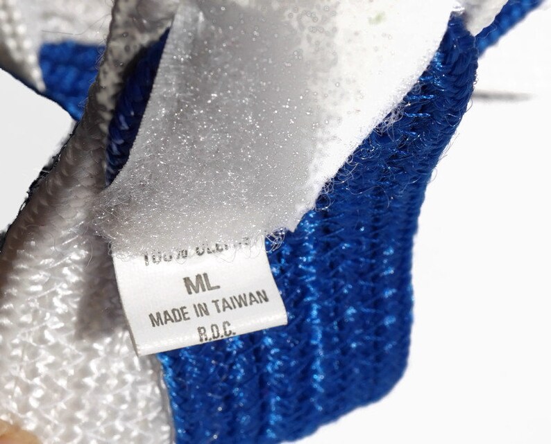May include: Close-up of a white and blue knitted textile. A white label with black text reads "100% OLEFIN", "ML", "MADE IN TAIWAN R.O.C.". The textile has a textured appearance with a blue border.