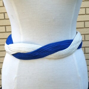 May include: A blue and white braided belt is wrapped around a white form. The belt is made of a woven material, with the blue and white sections intertwined. The belt is a stylish accessory.