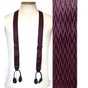 May include: Burgundy suspenders with a repeating geometric pattern. The suspenders have black leather button attachments and metal adjusters. The fabric has a textured appearance. The suspenders are displayed on a white mannequin.