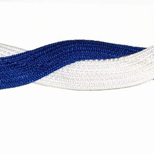 May include: A braided headband featuring a woven design in white and royal blue. The headband is twisted, creating a visually appealing pattern. The accessory is likely for hair styling.