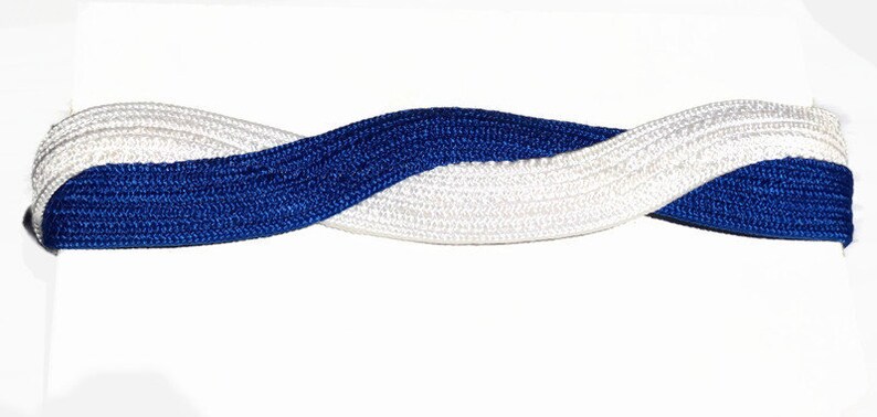 May include: A braided headband featuring a woven design in white and royal blue. The headband is twisted, creating a visually appealing pattern. The accessory is likely for hair styling.
