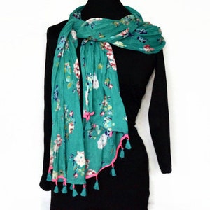 May include: A teal scarf with a floral pattern in white, pink, and blue. The scarf has a pink trim and tassels. The scarf is draped over a black dress form.