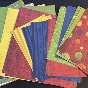 Puede incluir: Una pila de hojas de papel con patrones coloridos con un esquema de color rojo, amarillo, verde y azul. Las hojas de papel tienen diferentes patrones, incluyendo lunares, rayas y remolinos. Las hojas de papel están dispuestas en forma de abanico. Las hojas de papel son para scrapbooking, creación de tarjetas y otras manualidades de papel.