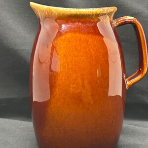 May include: A brown ceramic pitcher with a wide mouth and a handle. The pitcher has a glazed finish and a light brown rim.