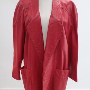 May include: A bright red leather blazer featuring a wide notched lapel, long sleeves, and two large patch pockets on the front. The jacket has a relaxed, oversized fit with structured shoulders and a smooth, solid red finish throughout the garment.