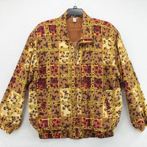 May include: A vintage zip-up jacket with a brown, gold, and red geometric pattern. The jacket features a repeating design of squares, chains, and floral motifs. The brand name "FUDA" is visible on the collar. The jacket has long sleeves and a relaxed fit.