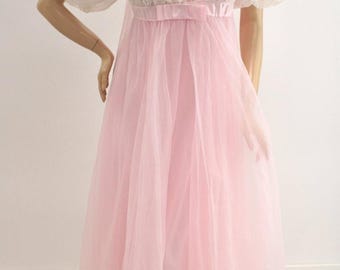 May include: A floor-length nightgown featuring a sheer white lace bodice with short puff sleeves and a ruffled neckline. The waist is accented with a pink satin ribbon bow, transitioning into a flowing, layered pink tulle skirt.