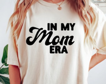 May include: A white t-shirt with black text that reads "In My Mom Era".